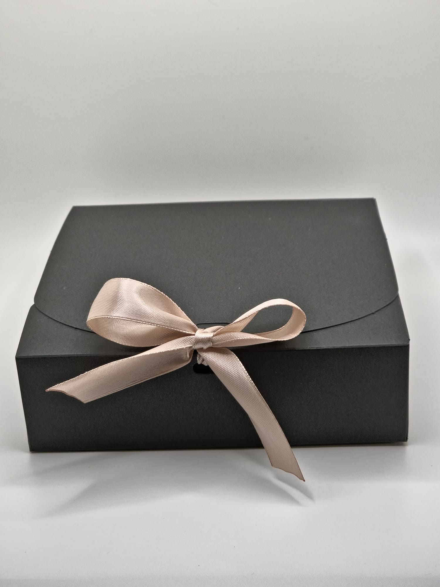 Black gift box with a beige ribbon on a light gray background